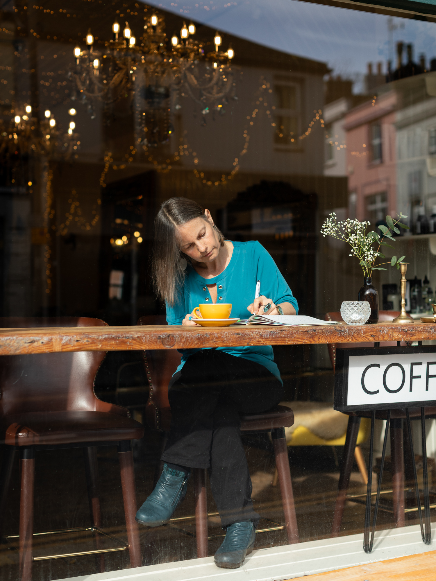Nicky Torode writing in a journal at a cafe window